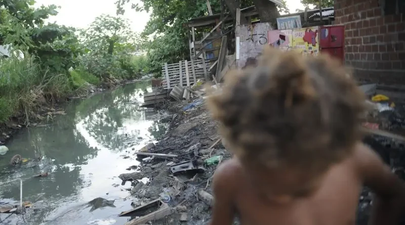 Imagem de riacho com falta de saneamento básico e uma criança passando em favela do Complexo da Maré