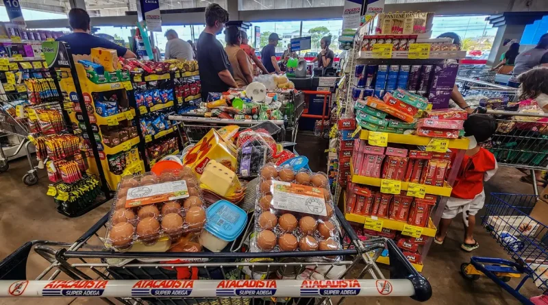 12/06/2026 - Brasília - Consumidores enfrentam longas filas nos caixas de um grande mercado atacadista para finalizar suas compras. Diante do cenário de inflação acumulada e da constante alta de preços nos itens básicos de alimentação, a busca por qualquer tipo de desconto ou promoção tornou-se estratégia essencial para aliviar o orçamento das famílias.Foto: Rafa Neddermeyer/Agência Brasil